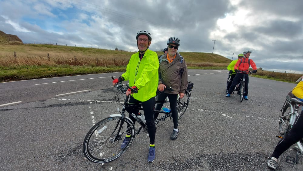 Lee and Chris smiling on a tandem at a rest stop